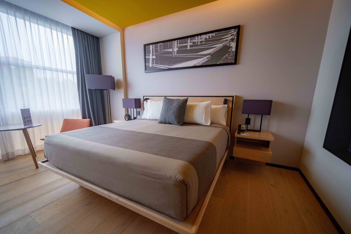 Una habitación de hotel moderna con una cama grande, mesitas de noche, un escritorio y una ventana con cortinas.