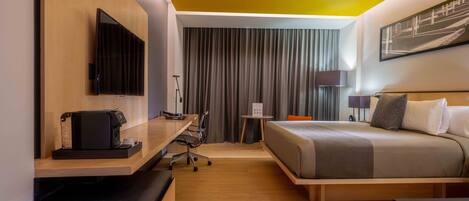 A hotel room with a bed, a desk with a computer, a TV, and a window with curtains.