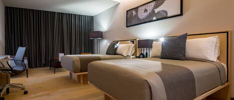 A hotel room with two beds, a desk, a chair, and a large window with curtains.