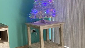 A small wooden table with a decorative Christmas tree on top, positioned against a teal wall and a striped curtain. - Linda Vista 106 (2Bedroom-2Bathroom) By FMI Rentals (Puerto Peñasco)
