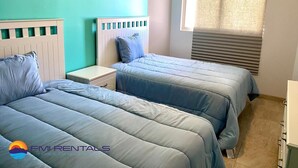 A room with two beds, a window with blinds, a nightstand, and a dresser. - Linda Vista 106 (2Bedroom-2Bathroom) By FMI Rentals (Puerto Peñasco)