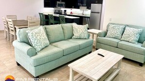 A modern living room with two green sofas, a wooden coffee table, and a dining area with a wooden table and chairs. - Linda Vista 106 (2Bedroom-2Bathroom) By FMI Rentals (Puerto Peñasco)