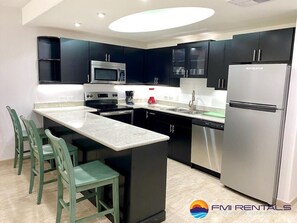A modern kitchen with dark cabinets, a stainless steel refrigerator, and a central island with chairs.
