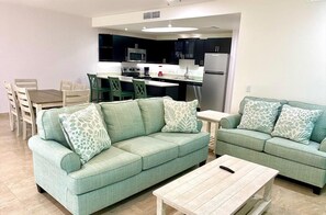 Una sala de estar moderna con dos sofás verdes, una mesa de centro de madera y un comedor con una mesa y sillas de madera.