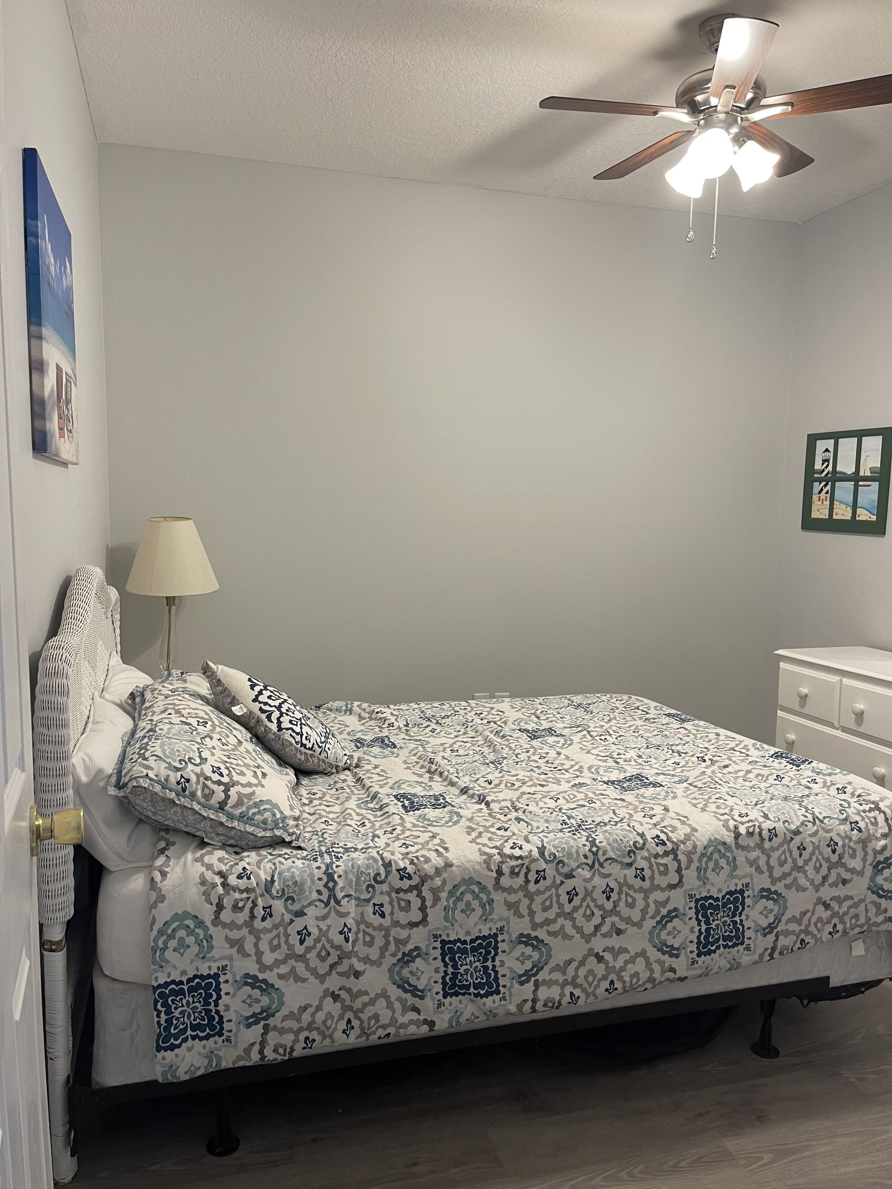 Ein Schlafzimmer mit einem Bett, einem Deckenventilator, einem Nachttisch, einer Lampe und einem Bild an der Wand.