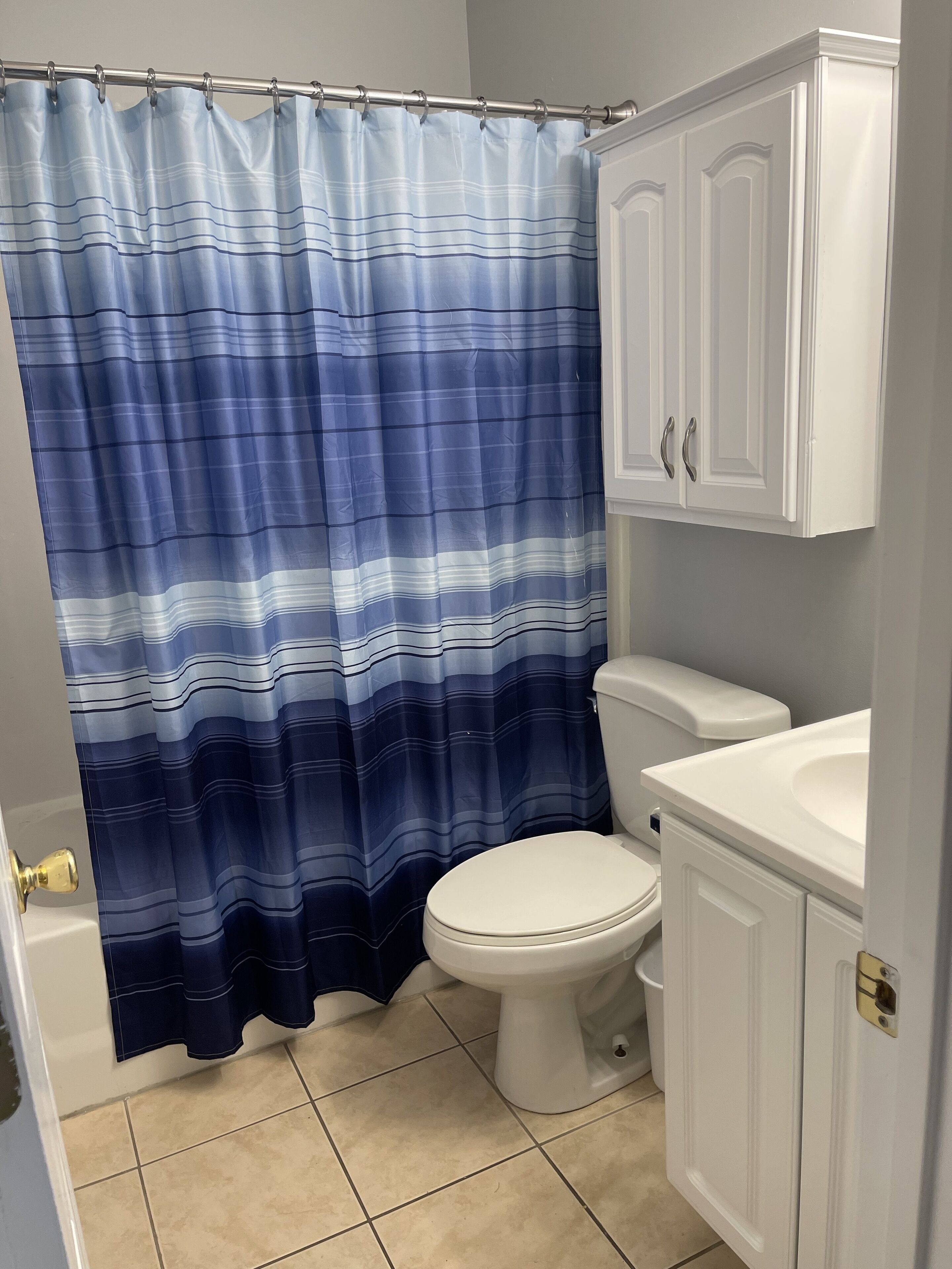 Un baño con cortina de ducha a rayas, un inodoro, un lavabo y un armario.