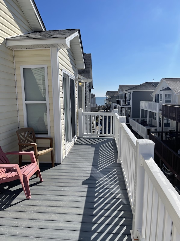A wooden deck with white railings, a chair, and a view of the ocean.