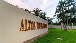 Ein Schild mit dem Schriftzug "ALTOS DE LA MAJORCA" an einer weißen Wand, umgeben von einer gepflegten Grünfläche und Palmen.