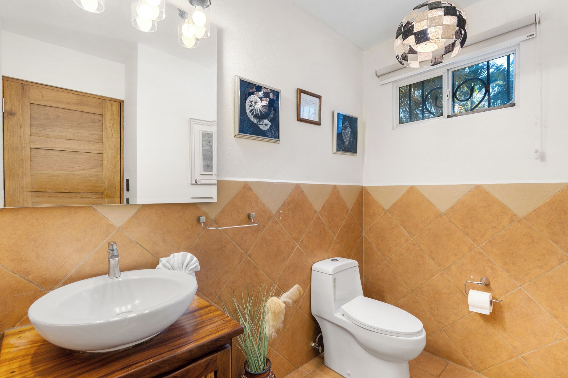 A bathroom with a wooden vanity, a white sink, a toilet, and a decorative ceiling light.