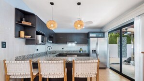 A modern kitchen with a central island, dark cabinetry, and a large window. - Spacious Home w/ Private Pool & Covered Patio Near the Beach (Tempate)