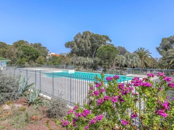 A swimming pool surrounded by a metal fence, with purple flowers in the foreground and trees in the background. - Le Grand Parc by Interhome (Saint Aygulf)