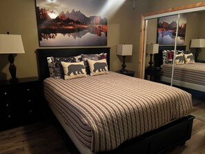 Een slaapkamer met een groot bed, twee nachtkastjes, een spiegel en een schilderij van een berglandschap.