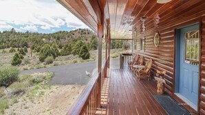 Una cabaña de madera con un porche que da a una carretera y un área boscosa.