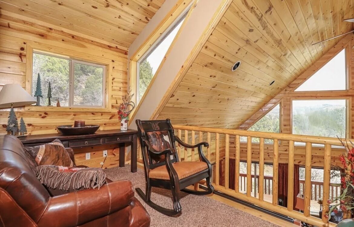 Un chalet confortable avec un intérieur en bois, un fauteuil à bascule, un canapé en cuir et de grandes fenêtres donnant sur le paysage extérieur.