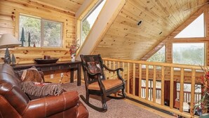 Una cabaña acogedora con interior de madera, una mecedora, un sofá de cuero y grandes ventanales que ofrecen vistas al exterior.