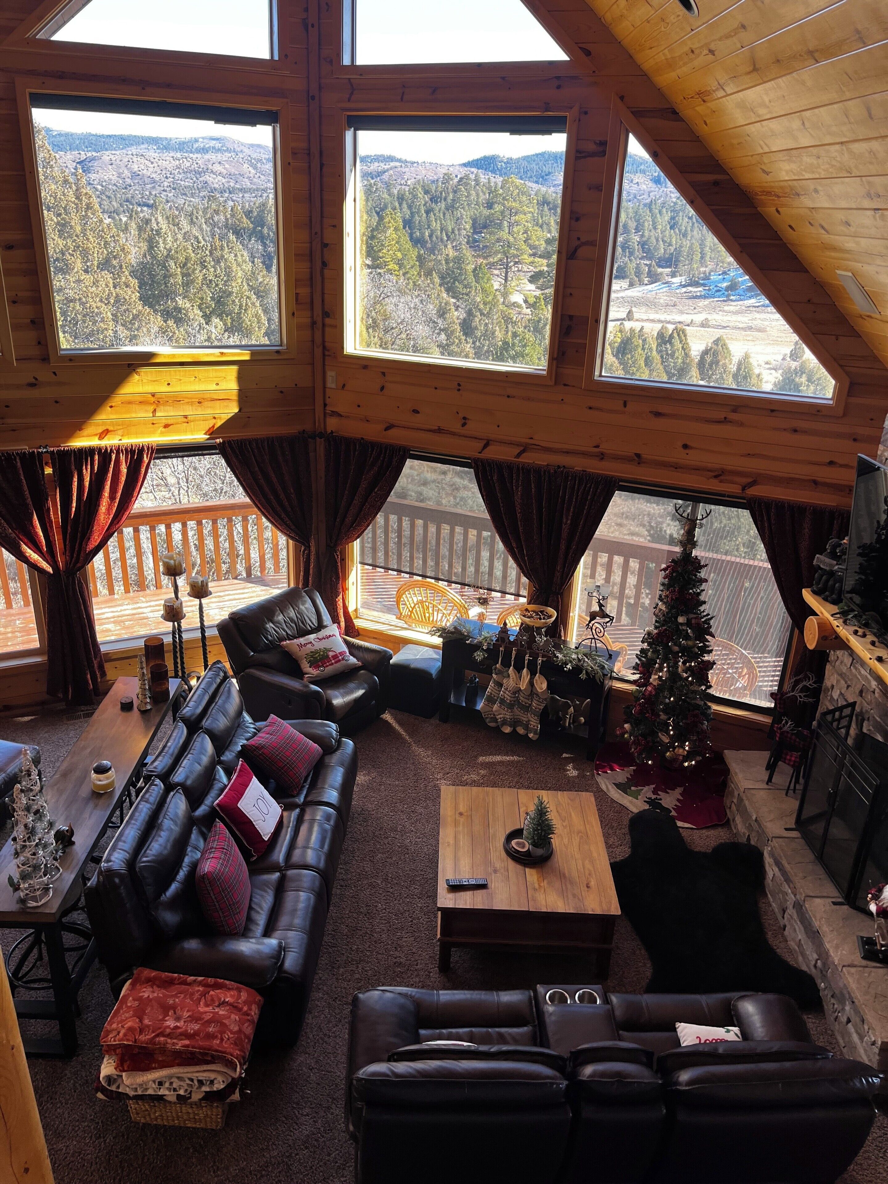 A cozy cabin interior with a large wooden ceiling, a leather sofa, a coffee table, and a Christmas tree.