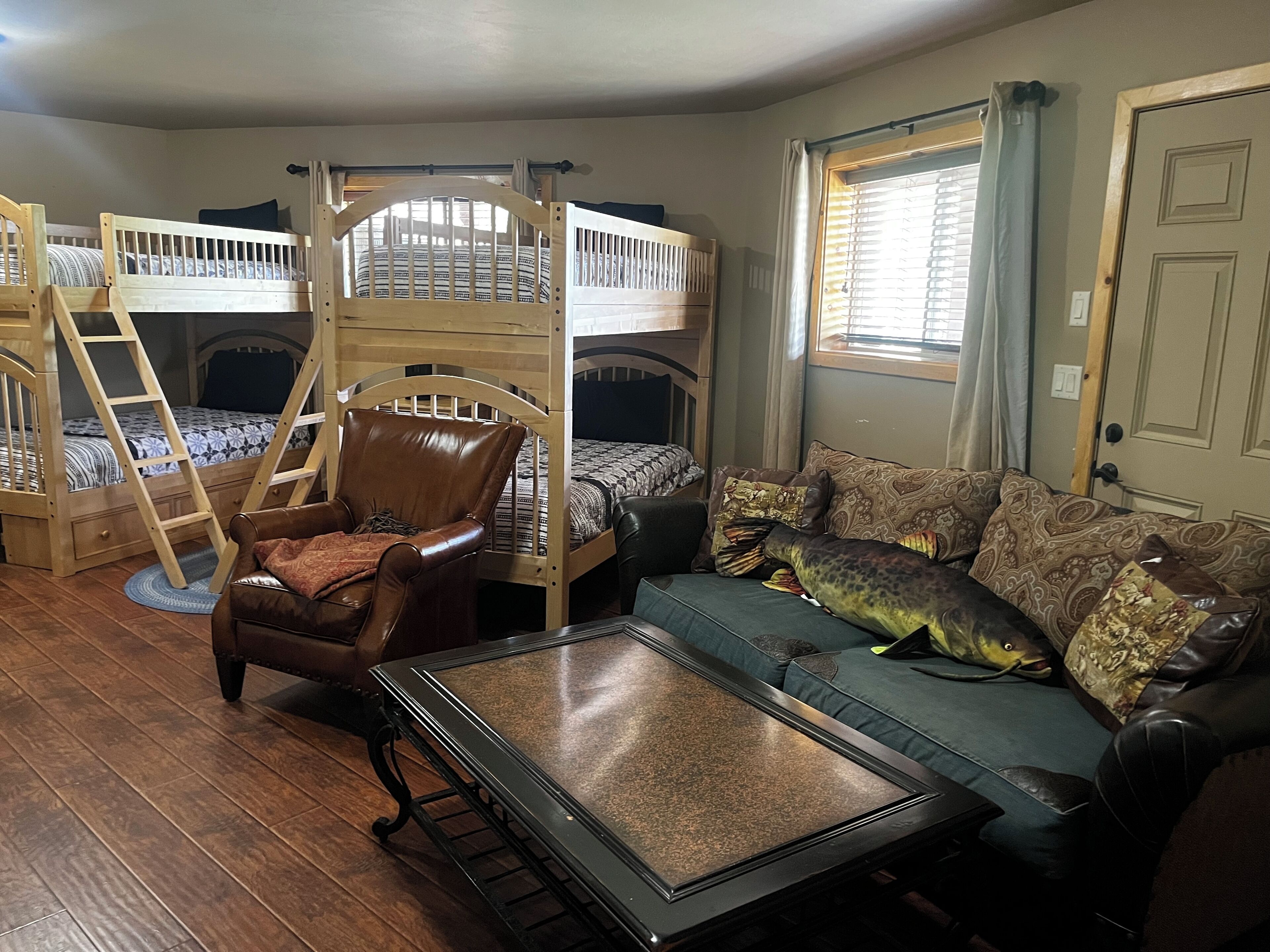 Una habitación con literas, un sillón de cuero, una mesa de centro de vidrio y un sofá con cojines estampados.