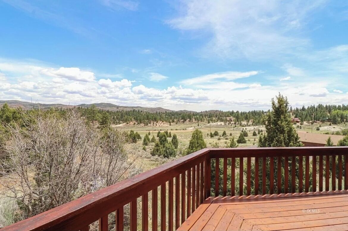 A wooden deck with a view of a rural landscape, including fields, trees, and distant hills.
