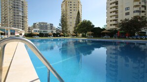 Una piscina con una scala in metallo, circondata da alti edifici residenziali e alberi.