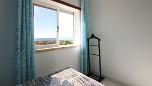 Una camera da letto con un letto, una finestra con tende e vista sul mare.