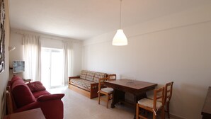 A living room with a sofa, a dining table, and chairs. There is a television on the wall and a window with curtains. - Holiday apartment, sea-front, fantastic sea views. (Armação de Pêra)