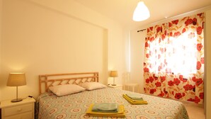 A bedroom with a bed, two bedside tables, a lamp, and a window with floral curtains. - Holiday apartment, sea-front, fantastic sea views. (Armação de Pêra)