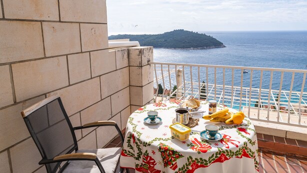 A balcony with a table set for breakfast, overlooking the sea and a distant island.