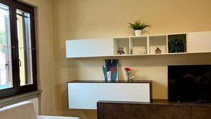 A modern living room with a sofa, a flat-screen TV, and a minimalist shelving unit with decorative items. - Bnbook - La Corte di Gallarate (Gallarate)