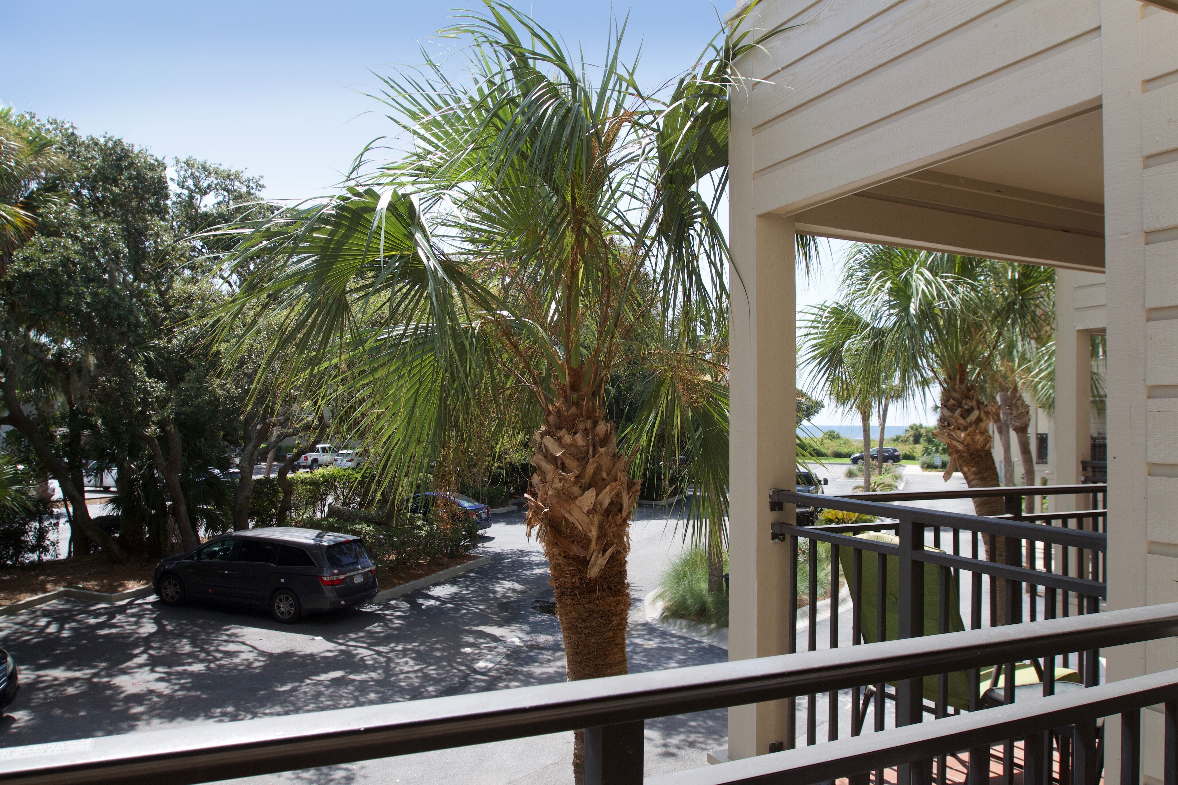 A residential area with a parked car, palm trees, and a house with a balcony.