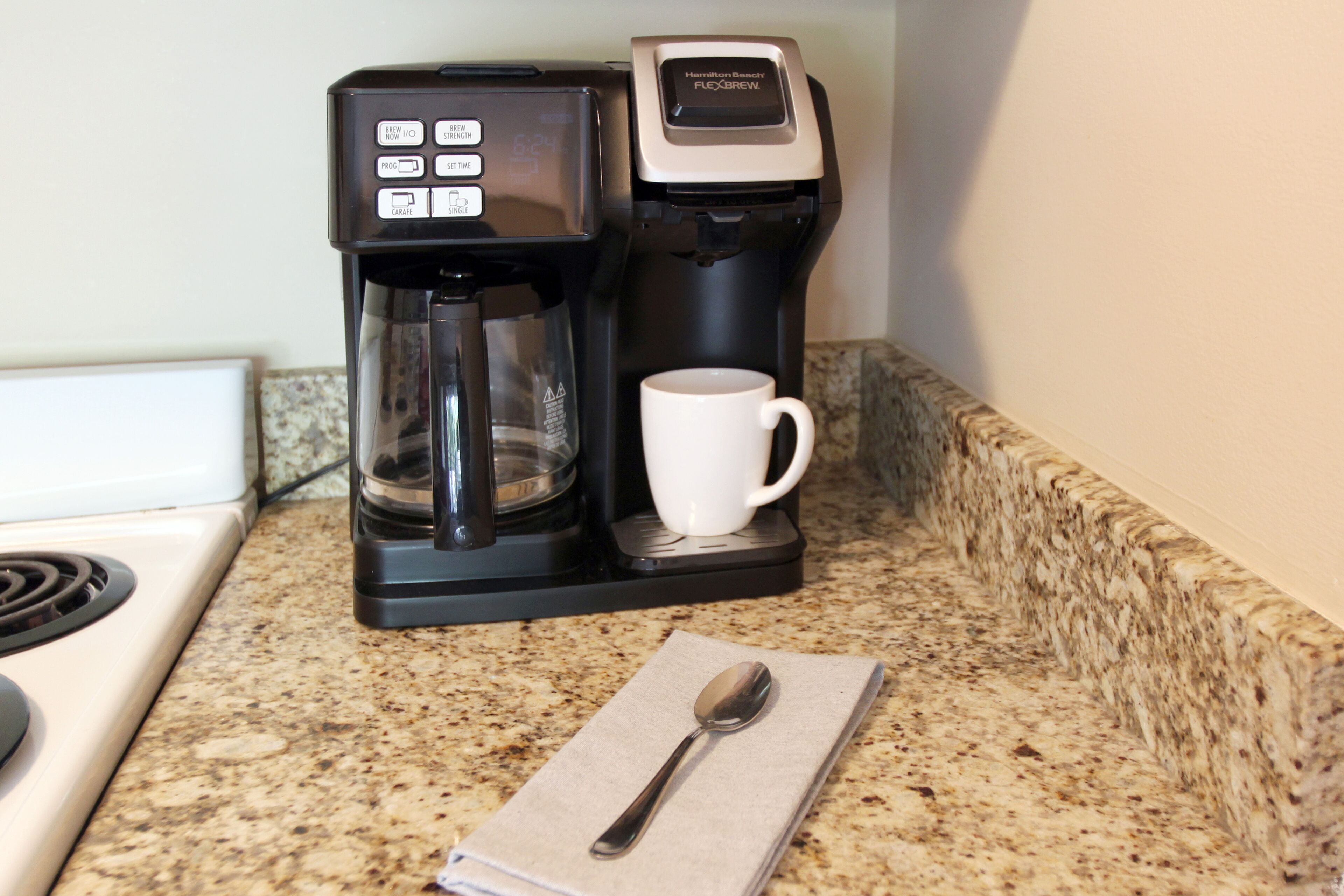 A coffee maker with a digital display and a cup on a granite countertop.