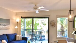 Ein Wohnzimmer mit einem blauen Sofa, einem kleinen Tisch, einem Deckenventilator und einem Balkon mit Stühlen und einem Tisch.