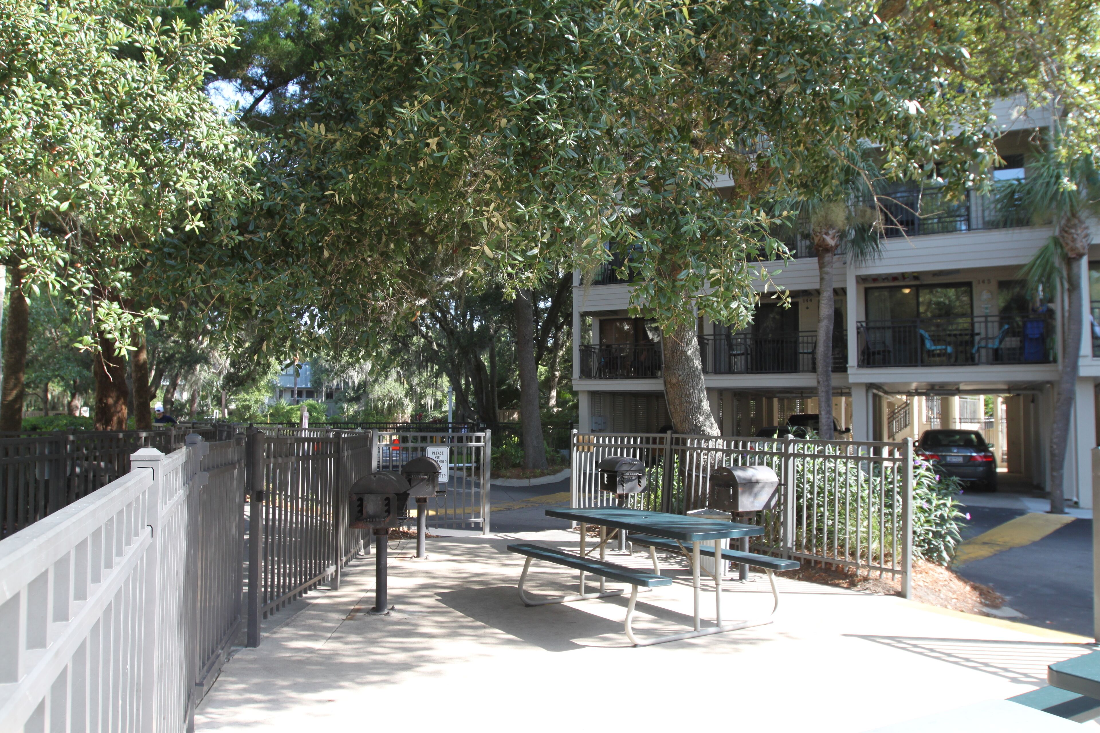 A park with picnic tables, a fence, and a building in the background.