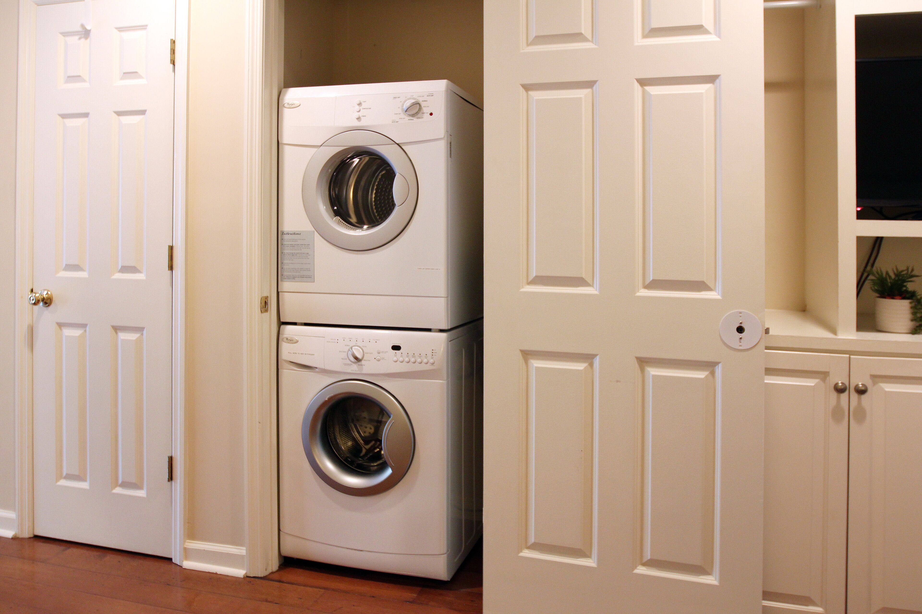 A laundry room with two stacked front-loading washing machines, a door, and a cabinet with a television above it.