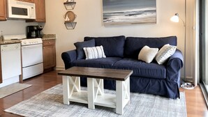 Ein Wohnzimmer mit einem dunkelblauen Sofa, einem Holztisch und einem Gemälde mit Strandmotiv.