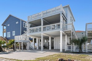 Una propiedad frente a la playa con un edificio de dos pisos, un porche cubierto y una escalera que lleva al nivel superior.