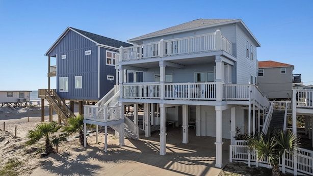 Ein Anwesen direkt am Strand mit einem zweistöckigen Haus, einem Balkon und einem separaten Holzgebäude.