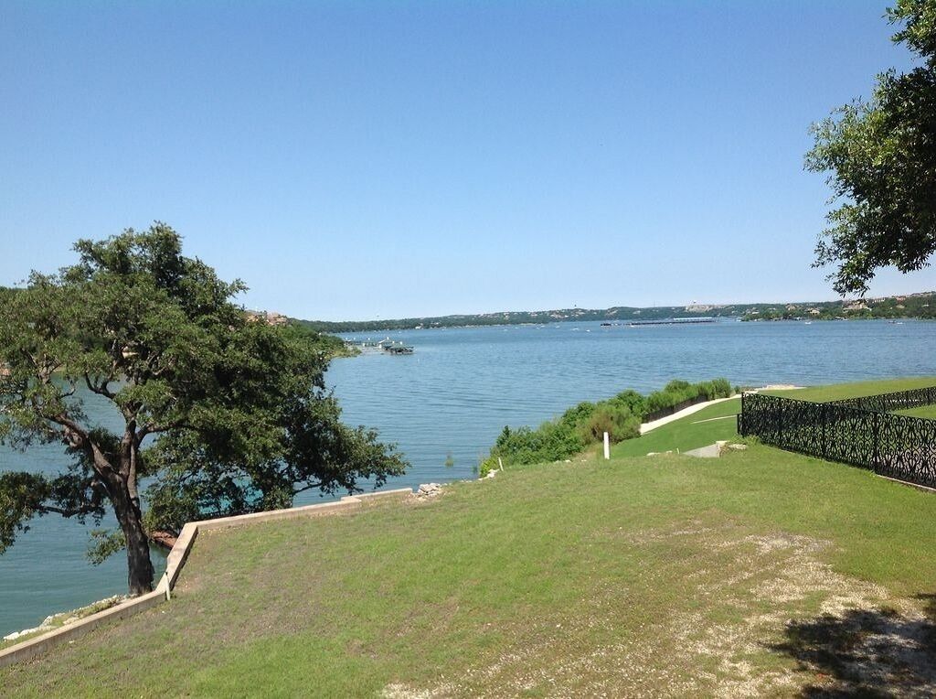 A grassy area with a body of water, a tree, and a fence.