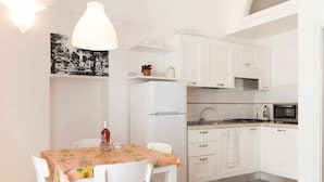 A compact kitchen with white cabinets, a refrigerator, a microwave, and a dining area with a table and chairs. - WePuglia - Sogno di Mezza Estate - Apt. Fattoi (Polignano a Mare)
