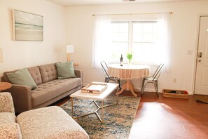 Ein Wohnzimmer mit einer Couch, einem Couchtisch, einem Esstisch mit Stühlen und einem Fenster mit Vorhängen.
