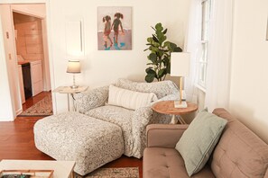 Ein gemütliches Wohnzimmer mit einer Couch, einem Couchtisch und einer Lampe. An der Wand hängt ein Bild und in der Ecke steht eine Pflanze.