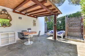 Un patio couvert avec un sol en pierre, une table en bois, deux chaises, une étagère blanche et un miroir décoratif.