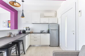 Une cuisine compacte avec des meubles blancs, un réfrigérateur en acier inoxydable, une machine à café et un tabouret de bar.