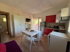 A compact kitchen with white and red cabinets, a white dining table with chairs, a refrigerator, a microwave, and a television on the wall. - Holiday Home "Villetta Lampone" with Air Conditioning, Garden and Terrace (CAPOLIVERI - LACONA)