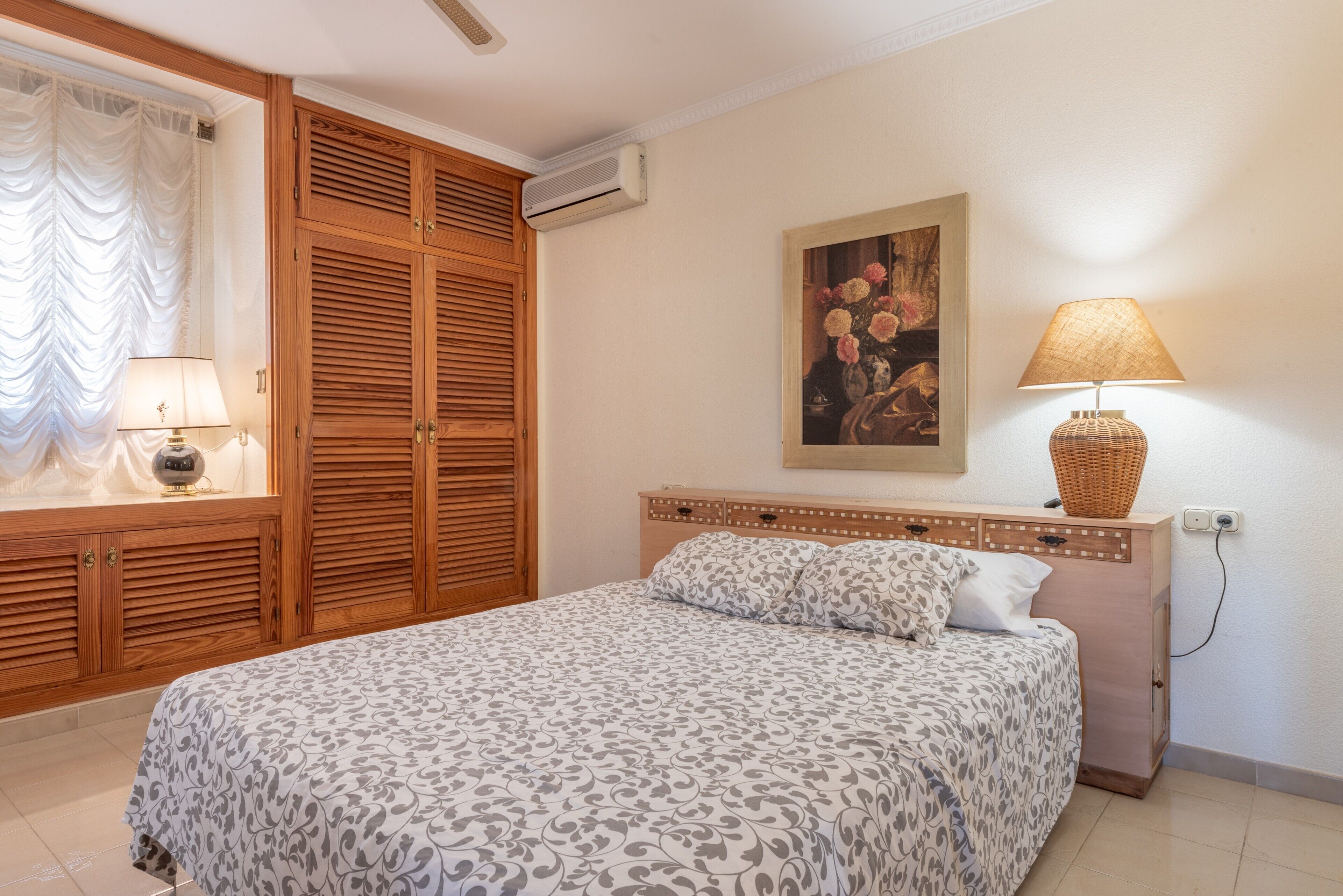 A bedroom with a bed, a bedside lamp, a painting, and a wardrobe.