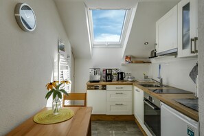 A compact kitchen with a skylight, a dining table with a vase of flowers, and white cabinetry.