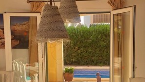 Un espace repas avec une longue table, des chaises, des luminaires suspendus et une vue sur la mer grâce à des portes vitrées.