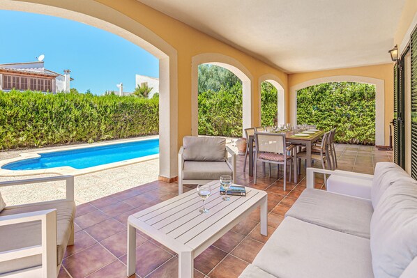A covered outdoor area with a pool, seating, and a table set for dining.