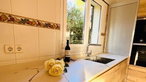 Une cuisine avec des armoires blanches, une fenêtre, un évier et une bouteille de vin posée sur le comptoir.