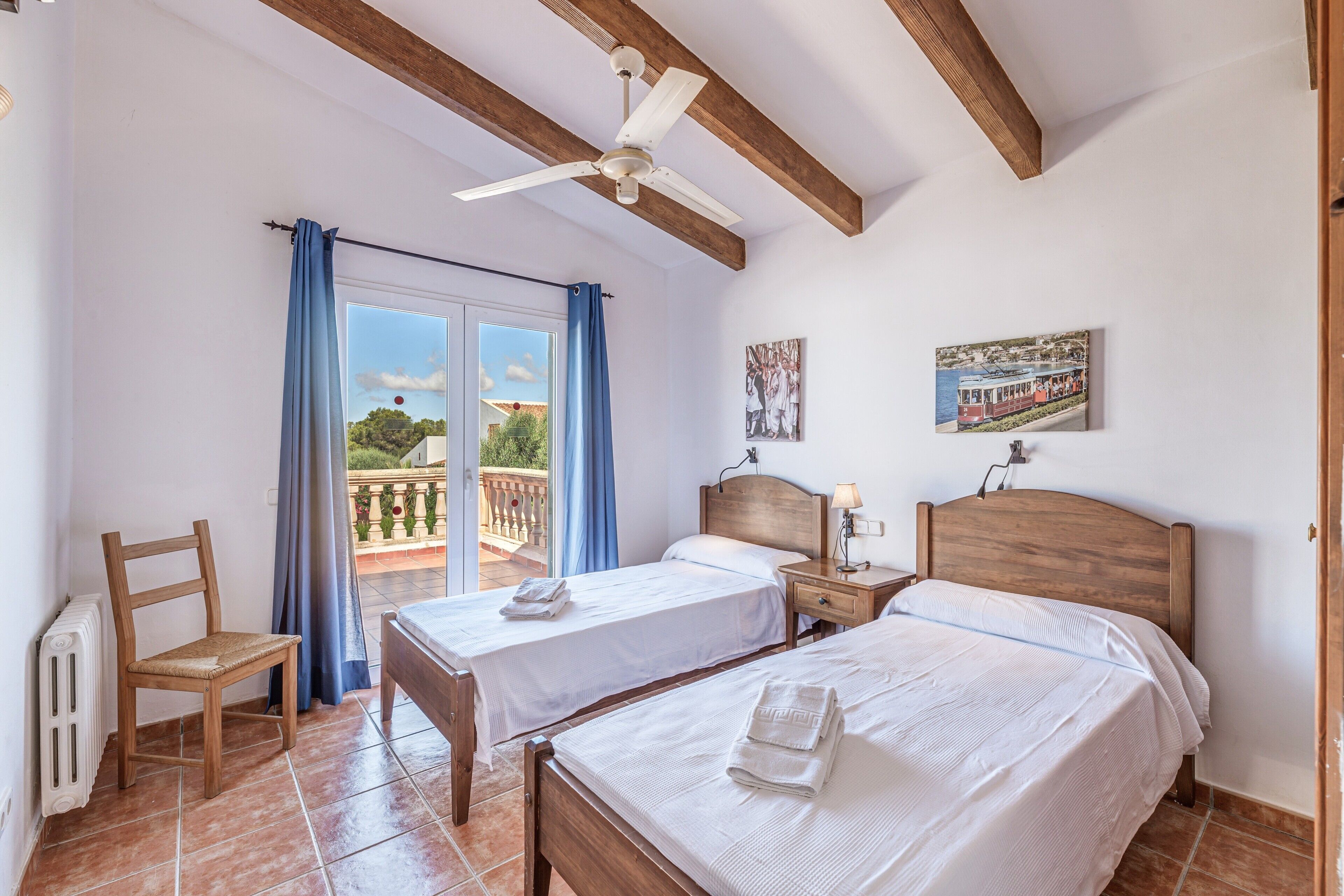 A bedroom with two beds, a chair, a ceiling fan, and a balcony with a view.
