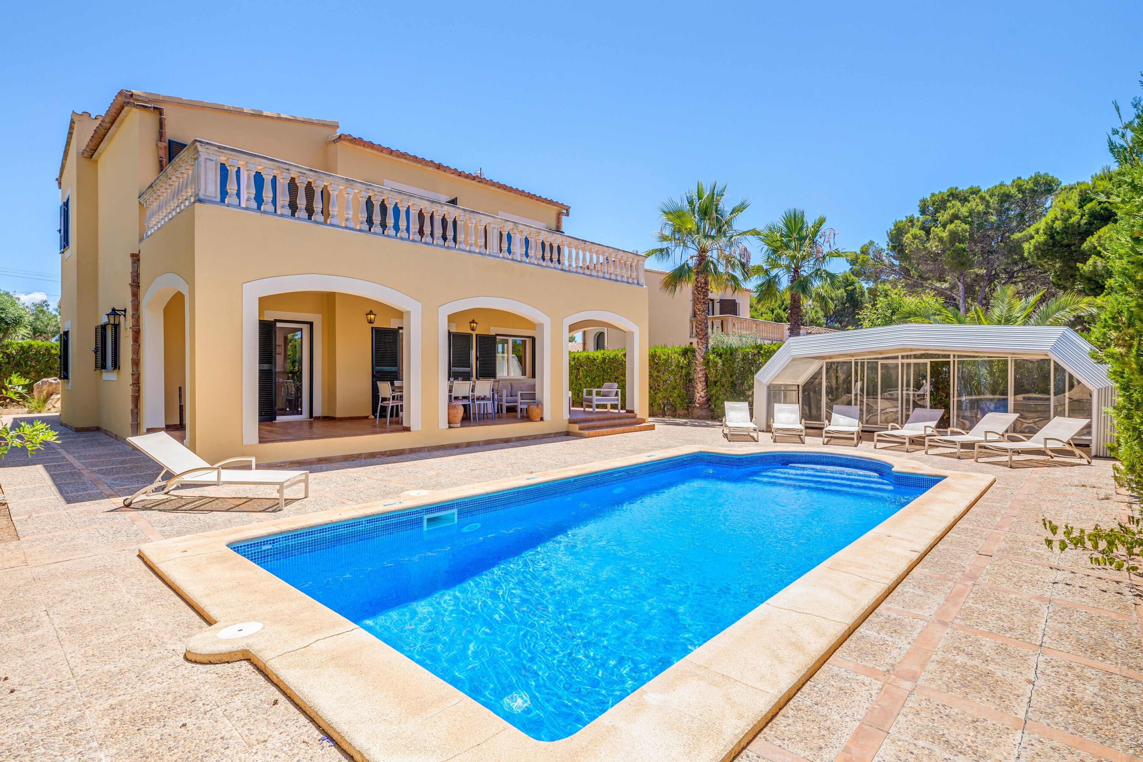 Una casa de dos pisos con piscina, mobiliario de exterior y un espacio cubierto.
